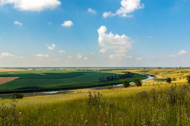 Mavi gökyüzündeki tepeden güzel bir manzara, ufuktan uzanan nehir ve tarım alanları.
