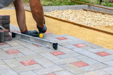 Eldivenli bir zanaatkar lastik bir çekiçle çakıllı bir kum tabanına beton bloklar yerleştirir. Kaldırıma beton bloklar döşemek.