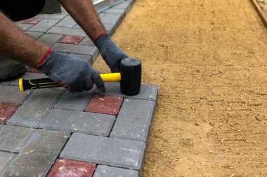 Eldiven giymiş, lastik çekiçle beton bloklar döşeyen bir işçinin elleri..
