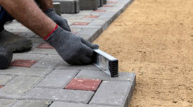 Eldiven giymiş, lastik çekiçle beton bloklar döşeyen bir işçinin elleri.