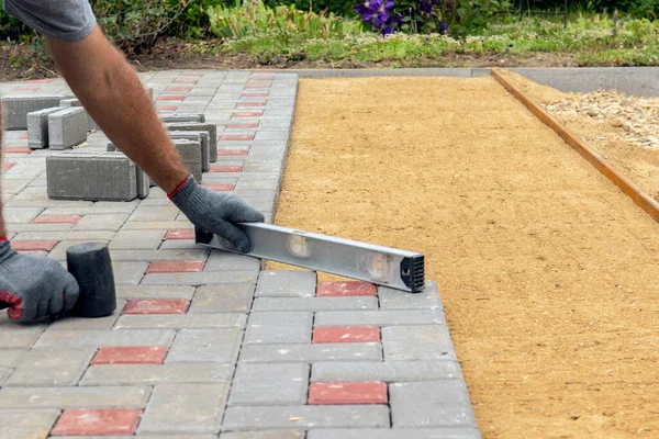 Hands of a worker in gloves laying concrete blocks with a rubber hammer.