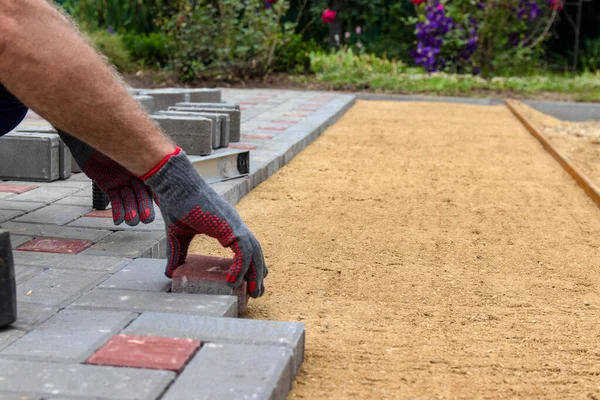 Eldivenli bir zanaatkar lastik bir çekiçle çakıllı bir kum tabanına beton bloklar yerleştirir. Eldivenli bir zanaatkar lastik bir çekiçle çakıllı bir kum tabanına beton bloklar yerleştirir. Kaldırıma beton bloklar döşemek