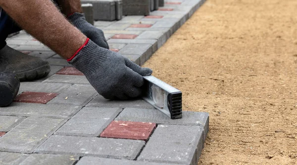 Hands of a worker in gloves laying concrete blocks with a rubber hammer