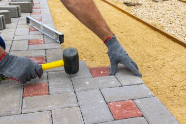 Bir inşaat işçisi, bir kır evinin avlusuna kaldırımlar için beton bloklar kuruyor.