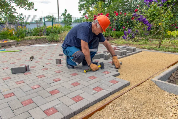 Profesyonel tuğla ustaları yol, kaldırım ya da veranda için yeni kiremitler ya da levhalar döşüyorlar. Evin avlusuna gri beton döşeme döşemesi.
