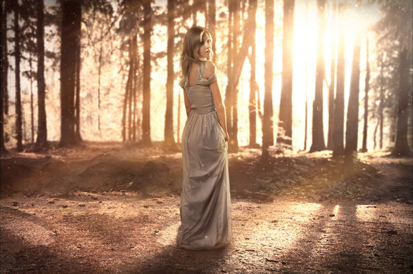 Woman in a dress stands on a mystical glade in a magical forest