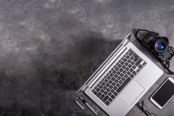 Composition of a laptop, camera, phone, glasses and a pen on a stone counter