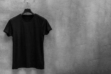 Erkek siyah ön yüzü pamuk t-shirt bir askı ve beton duvar içinde belgili tanımlık geçmiş. T-shirt baskı ve boşaltmak için metninizi sağ tarafında olmadan
