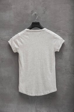 Kadın gri melanj tarafına geri pamuk t-shirt bir askı ve beton duvar içinde belgili tanımlık geçmiş. T-shirt baskı olmadan