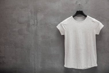 Kadın gri melanj ön yüzü pamuk t-shirt bir askı ve beton duvar içinde belgili tanımlık geçmiş. T-shirt baskı ve boşaltmak için sol taraftaki metin olmadan