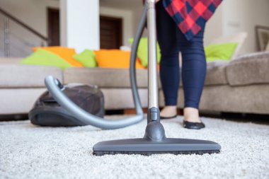 Woman is cleaning up the light grey carpet with vacuum cleaner w