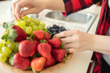 Woman puts green grapes, strawberries and blueberries in wooden 