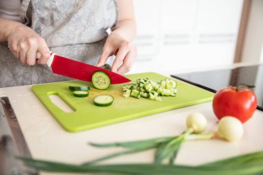 Woman in  kitchen apron cuts cucumber on the cutting board with 
