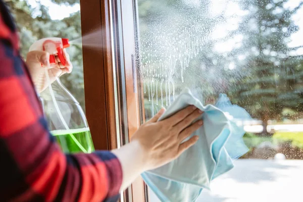 Woman is splashing cleaning liquid on the window with garden in — 스톡 사진