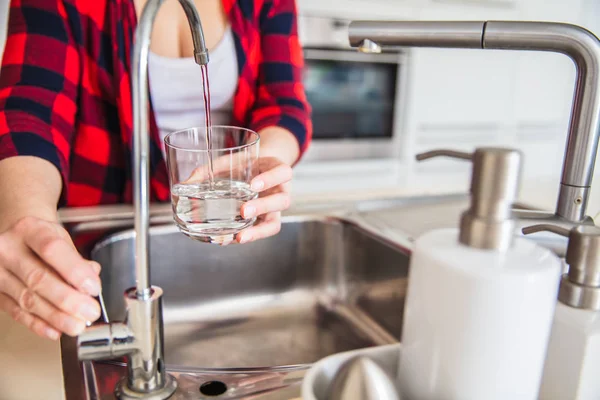 Женщина наливает воду из раковины в стекло на кухне — стоковое фото