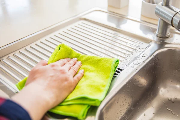 Woman is wiping the water from the drainer in the kitchen with g — Stock Photo, Image