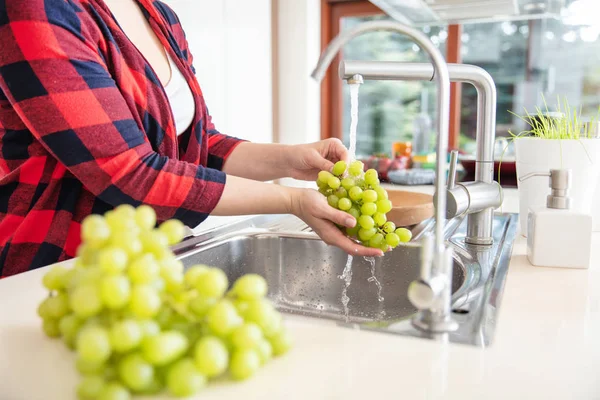 Woman is rinsing the green grapes with water in the kitchen and — Stok fotoğraf