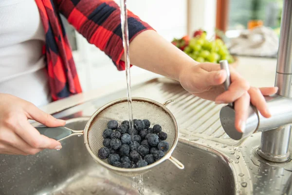 Woman rinses blueberries on the strainer with water in the kitch — Stok fotoğraf