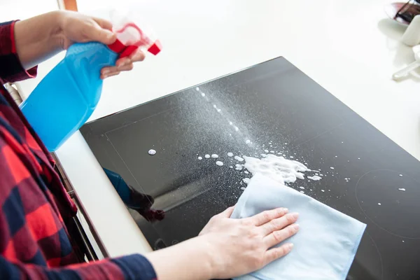 Woman splashes cleaning foam from blue bottle on the induction h — Stockfoto