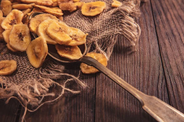 Plátanos secos apilados en una tela y cuchara sobre una vieja mesa marrón — Foto de Stock