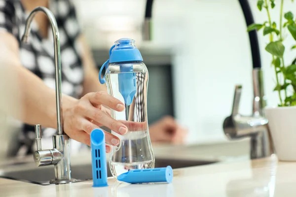 Yedek karbon filtreli yeniden kullanılabilir su şişesi. Kadının eli, lavabodan yeniden kullanılabilir temiz su şişesini karbon filtresiyle kaplıyor ve ön tarafta iki tane yedek karbon filtresi bulunuyor.