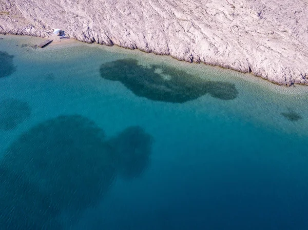 Aerial view of a trendy tent, cover from the sun. Rocks on the sea and transparent sea floor. Relax and vacation under a white tent surrounded by rocks on the sea.  Rucica beach on the island of Pag, Metajna, Croatia