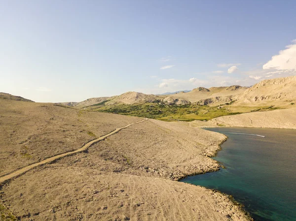 Aerial view of a winding road that runs along the Croatian coasts, dirt road, island of Pag near Rucica beach in Metajna. Wild and uncontaminated nature. Transparent sea. Croatia