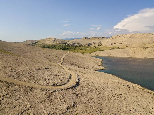 Aerial view of a winding road that runs along the Croatian coasts, dirt road, island of Pag near Rucica beach in Metajna. Wild and uncontaminated nature. Transparent sea. Croatia