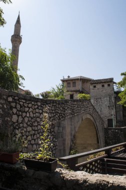 Bosna, 5/07/2018: Kriva Cuprija (Sloping Köprüsü), en eski tek kemer taş Köprüsü Mostar yerleşik 1558 Osmanlı mimarı Cejvan Kethoda ve Nezir agina dzamija camii minaresi