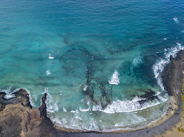 Aerial view of a crystal clear sea with waves and surfers. Playa De La Canteria. Atlantic Ocean, waves crashing on the beach at sunset, backlighting. Orzola, Lanzarote, Canary Islands. Spain