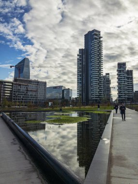 Ağaçlar, yeni Milan park Kütüphanesi. Solaryum panelleri tower. 11/07/2018. Gökdelenlerin panoramik manzaralı yolları Park. Çeşme yansıtılmış gökdelenler. Lombardy, İtalya