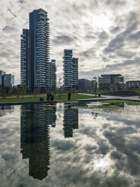 Ağaçlar, yeni Milan park Kütüphanesi. Solaryum panelleri tower. 11/07/2018. Gökdelenlerin panoramik manzaralı yolları Park. Çeşme yansıtılmış gökdelenler. Lombardy, İtalya