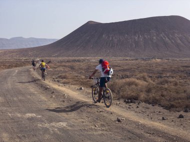 İnsanlar La Graciosa Island, Lanzarote, Kanarya Adaları'nda bir toprak yolda Bisiklete binme. İspanya. Arka plan El risco, Lanzarote dağlık parçası Kuzey