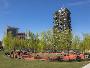Ağaçlar, banklar ve hali ile dinlenme alanı Kütüphanesi. İnsanlar etrafta dolaşan bir öğle yemeği molası. Ağlayan willows. Dikey orman Milan merkezinde yeni Parkı görüldü. 03/18/2019. İtalya