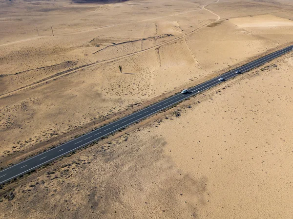 Aerial view of a desert landscape on the island of Lanzarote, Canary Islands, Spain. Road that crosses a desert. Tongue of black asphalt cutting a desert land. Reliefs on the horizon. Volcanoes.