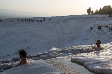 Türkiye, 07/10/2019: güneş batımında, Pamukkale 'de Traverten teraslarında (Cotton Castle), su tarafından yatırılan sedimanlı kayanın ünlü doğal alanı olan kaplıcalardan akan suyun tadını çıkaran erkekler