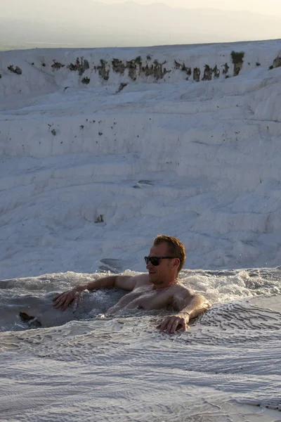 Türkiye, 07/10/2019: Pamukkale 'de Traverten teraslarında (pamuk Kalesi), su ile yatırılan sedimanlı kayanın ünlü doğal sitesi olan kaplıcalardan akan sudan zevk alan bir adam