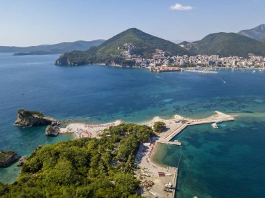 Sveti Nicola,Budva adasının havadan görünümü, Karadağ. Hawaii plajı, şemsiyeler, banyo yapanlar ve kristal berraklığında sular. Şeffaf denize bakan dik kayalıklar ile pürüzlü kıyıları. Vahşi doğa ve Akdeniz makileri