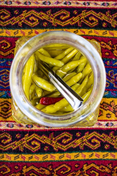 Middle Eastern food and lifestyle: a jar of spicy green chillies and hot pepper on a damask tablecloth