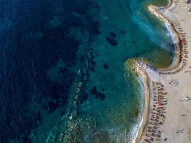Karadağ 'ın Budva adası Sveti Nikola' nın hava manzarası. Hawaii plajı, şemsiyeler, banyolar ve kristal berrak sular. Şeffaf denize bakan sarp kayalıkları olan sivri kıyılar. Vahşi doğa ve Akdeniz maketi