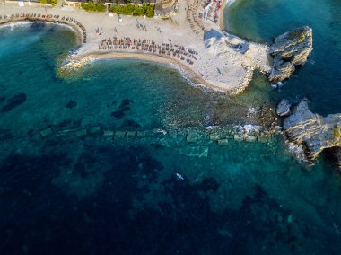 Karadağ 'ın Budva adası Sveti Nikola' nın hava manzarası. Hawaii plajı, şemsiyeler, banyolar ve kristal berrak sular. Şeffaf denize bakan sarp kayalıkları olan sivri kıyılar. Vahşi doğa ve Akdeniz maketi