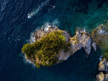 Karadağ 'ın Budva kentindeki Sveti Nikola adası yakınlarında uçan bir sürat teknesinin hava manzarası. Şeffaf denize bakan sarp kayalıkları olan sivri kıyılar. Vahşi doğa ve Akdeniz maketi