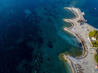 Karadağ 'ın Budva adası Sveti Nikola' nın hava manzarası. Hawaii plajı, şemsiyeler, banyolar ve kristal berrak sular. Şeffaf denize bakan sarp kayalıkları olan sivri kıyılar. Vahşi doğa ve Akdeniz maketi
