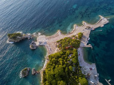 Karadağ 'ın Budva adası Sveti Nikola' nın hava manzarası. Hawaii plajı, şemsiyeler, banyolar ve kristal berrak sular. Şeffaf denize bakan sarp kayalıkları olan sivri kıyılar. Vahşi doğa ve Akdeniz maketi