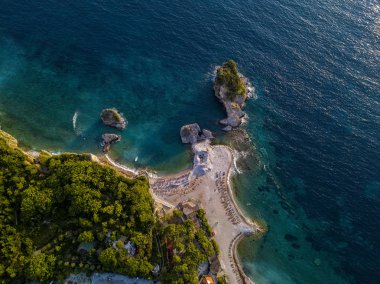 Karadağ 'ın Budva adası Sveti Nikola' nın hava manzarası. Hawaii plajı, şemsiyeler, banyolar ve kristal berrak sular. Şeffaf denize bakan sarp kayalıkları olan sivri kıyılar. Vahşi doğa ve Akdeniz maketi