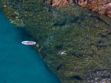 Şeffaf bir denizde yüzen, şnorkelle yüzen bir sörf tahtasının havadan görüntüsü. Denizde yıkanır. Tropea, Calabria, İtalya. Dalış ve yaz tatilleri. İtalyan kıyıları, plajları ve kayaları
