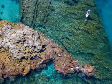 Şeffaf bir denizde yüzen, şnorkelle yüzen bir sörf tahtasının havadan görüntüsü. Denizde yıkanır. Tropea, Calabria, İtalya. Dalış ve yaz tatilleri. İtalyan kıyıları, plajları ve kayaları
