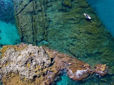 Şeffaf bir denizde yüzen, şnorkelle yüzen bir sörf tahtasının havadan görüntüsü. Denizde yıkanır. Tropea, Calabria, İtalya. Dalış ve yaz tatilleri. İtalyan kıyıları, plajları ve kayaları