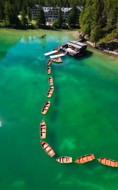 Pragser Wildsee, İtalya 'nın güneyindeki Prags Dolomites bölgesinde yer alan bir göldür. Sıraya dizilmiş sandalların görüntüsü. Arka planda otelin etrafı ağaçlarla çevrili.