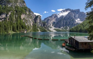 Panoramic view of the Lake Braies, Pragser Wildsee, lake in the Prags Dolomites, South Tyrol, Italy. Detail of rowboats moored in line on pristine water near a wooden cabin, mountains surrounded by trees. Covid free destinations clipart